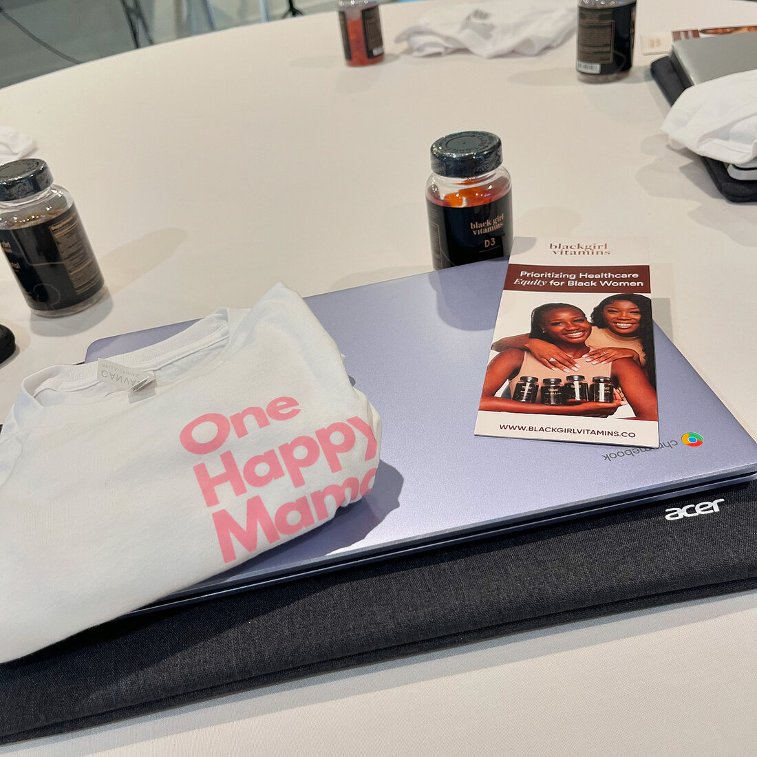 A One Happy Mama t-shirt, vitamins, a laptop and a health equity guide laid out for a mama